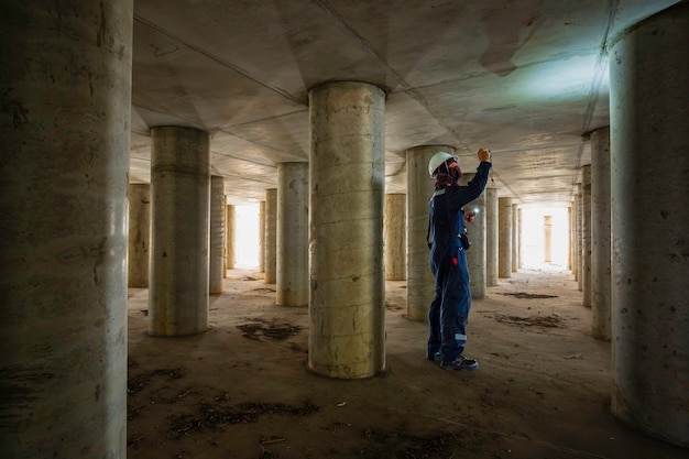 Zdjęcie działający męski słup inspekcyjny pod ziemią tunelu wyposażenia zbiornika za pomocą latarki wewnątrz pod zbiornikiem.