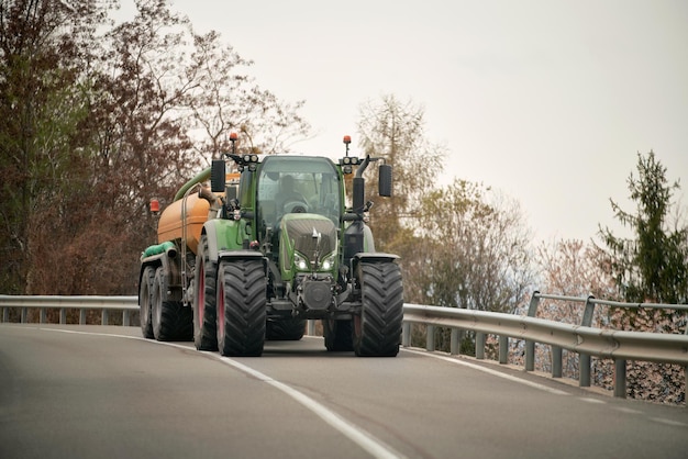 Działalność rolnicza w ruchu Traktor w pracy w słoneczny letni dzień Traktor rolniczy poruszający się po wiejskiej drodze w pobliżu gospodarstwa