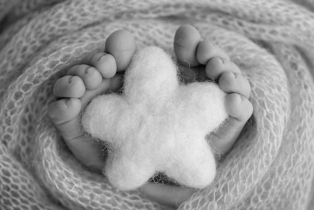 Dzianinowa gwiazda w nogach dziecka Miękkie stopy noworodka w wełnianym kocu Zbliżenie palców stóp, pięt i stóp noworodka Fotografia makro czarno-biała maleńka stopa noworodka