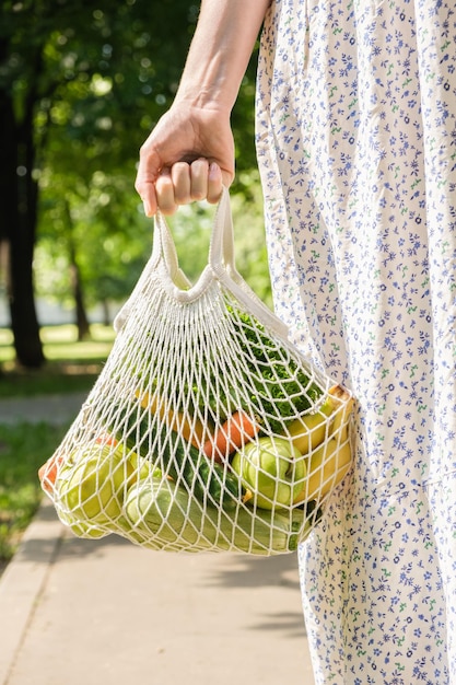 Dzianinowa siatkowa torebka z warzywami i owocami w rękach kobiety