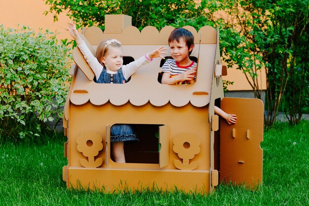 Zdjęcie dzieci bawią się w domku z kartonem, dzieci bawią się na świeżym powietrzu.