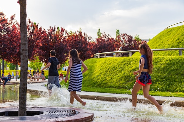 Dzieci bawiące się wodą w fontannie w parku. Gorące lato.