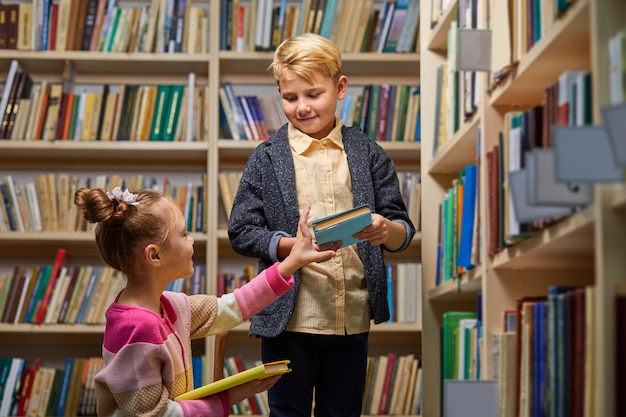 Dzieci chłopiec i dziewczynka wybierają książki w bibliotece do szkoły, idą czytać, zdobywać wiedzę