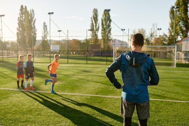 Dzieci ćwiczące piłkę nożną na boisku trawiastym pod kontrolą trenera piłki nożnej. Grupa młodych chłopców ćwiczących na stadionie w letni dzień