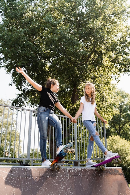 Dzieci dziewczyny jeżdżące razem na łyżwach Przyjaźń Przyjaciele gotowi do jazdy na deskorolce na deskorolce park plac zabaw Sprzęt sportowy dla dzieci Ekstremalny styl życia