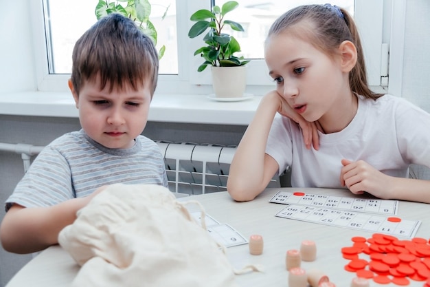 Zdjęcie dzieci grają w rosyjskie lotto na stole dziewczynka i chłopiec grają w grę planszową beczki z liczbami