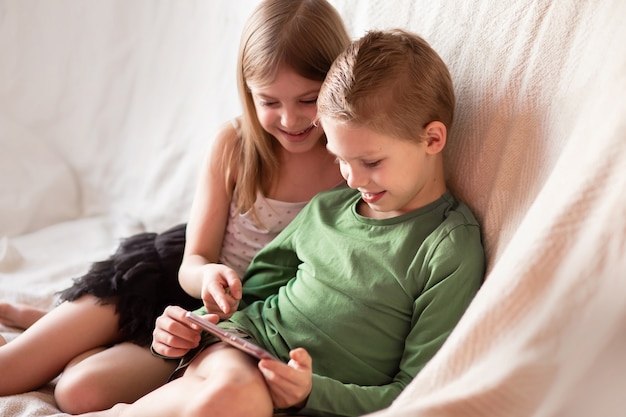 Zdjęcie dzieci grają w telefon, oglądają filmy na gadżetach leżących na kanapie