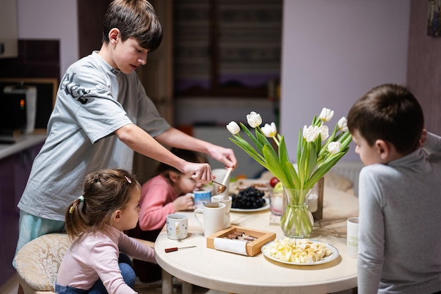 Dzieci jedzą owoce i desery piją herbatę w domu w wieczornej kuchni