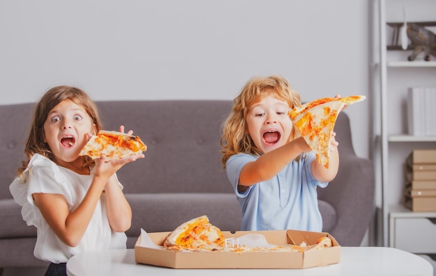 Dzieci jedzące pizzę podekscytowane dzieci jedzące pizzę dwoje małych dzieci gryzie pizzę w pomieszczeniu