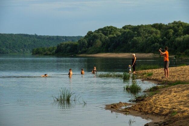 Zdjęcie dzieci kąpią się i łowią ryby na brzegu rzeki.