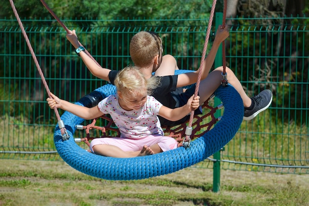 Dzieci na huśtawce chłopiec i dziewczynka jeżdżą na huśtawce w parku na letni dzień huśtawka w amu...