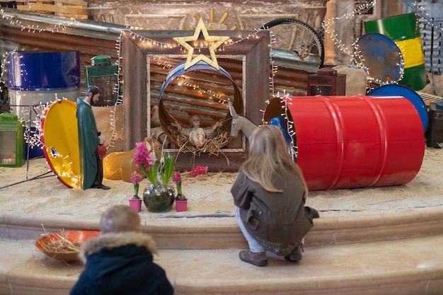 Zdjęcie dzieci patrzą na szopkę bożonarodzeniową z józefem maryją i małym jezusem w łóżeczku