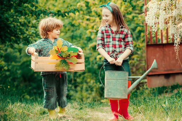 Dzieci rolników trzymają pudełko i konewkę urocza dziewczynka i chłopiec pracujący na farmie na zewnątrz