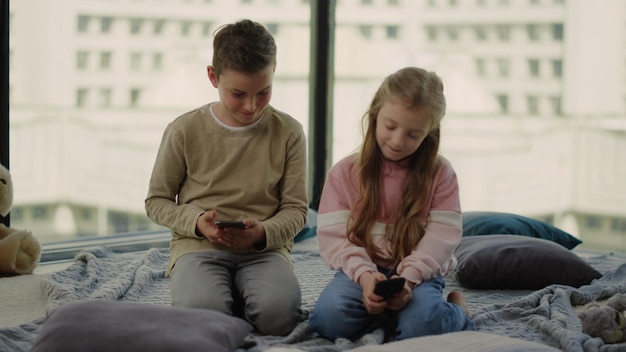 Dzieci siedzące na podłodze z telefonami komórkowymi Rodzeństwo grające w gry mobilne