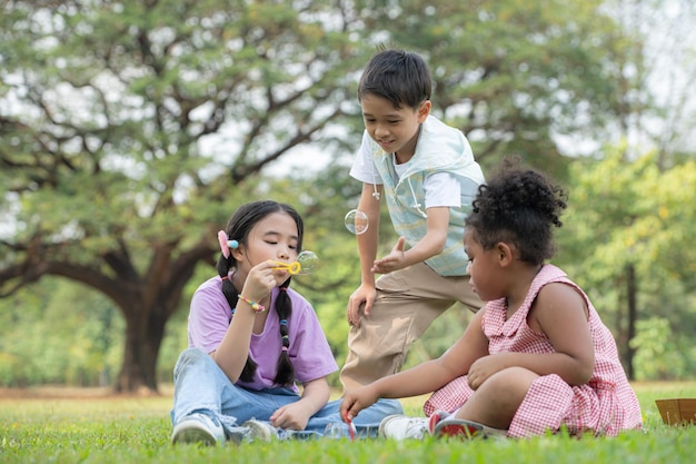 Dzieci siedzące w parku z pęcherzem powietrza, otoczone zielenią i naturą.
