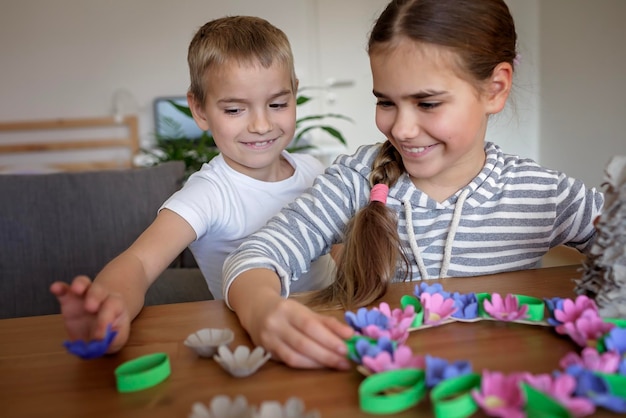 Zdjęcie dzieci tworzą wieniec z kwiatów wielkanocnych w pastelowych kolorach, korzystając ze stylu życia zero odpadów z recyklingu jajek