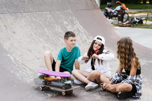 Dzieci Uśmiechają Się, śmieją I Bawią Się Razem Dzieci Z Deskorolką I Tabliczkami Groszy Komunikują Się I Dyskutują Na Sportowym Placu Zabaw Koncepcja Przyjaźni Chłopców I Dziewczynek