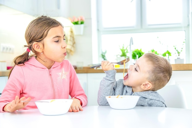 Dzieci w kuchni przy stole jedzą makaron