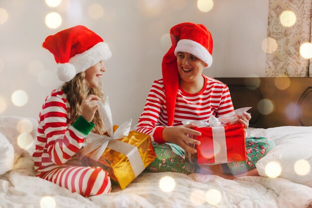 Dzieci w piżamach i świątecznych czapkach na łóżku z prezentami. koncepcja bożego narodzenia i nowego roku