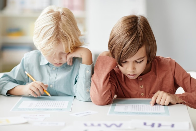 Zdjęcie dzieci w wieku szkolnym robiące notatki na papierze siedząc przy stole podczas lekcji