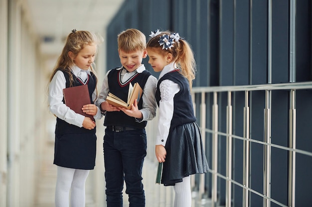 Dzieci w wieku szkolnym w mundurkach wraz z książkami na korytarzu Koncepcja edukacji