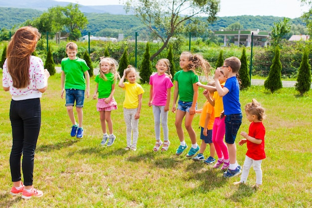 Dzieci z nauczycielem bawią się na świeżym powietrzu na zielonym trawniku. Dzieci stoją w rzędzie na trawie