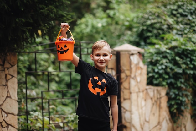 Dzieciak chłopiec nastolatek trzymający wiadro z dynią jackolantern z cukierkami i słodyczami Dzieciak lub psikus w święta Halloween