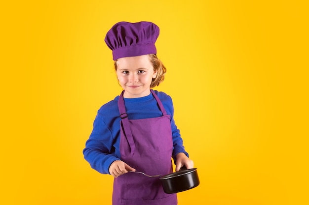 Dzieciak kucharz z garnkiem do gotowania Dziecko w mundurze kuchenki i kapeluszu szefa kuchni przygotowuje jedzenie na portrecie studia kuchennego Gotowanie kulinarne i koncepcja jedzenia dla dzieci
