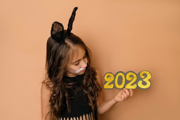 Dzieciak przebrany za czarnego królika trzyma w rękach złote numery nowego roku 2023