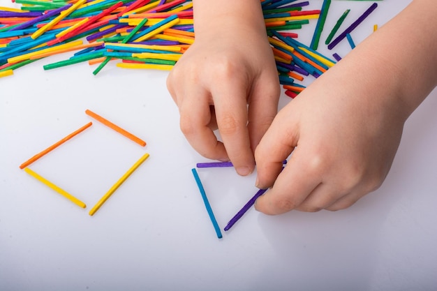Dzieciak robi geometrycznym kształtom z kolorowymi kijami na białym tle