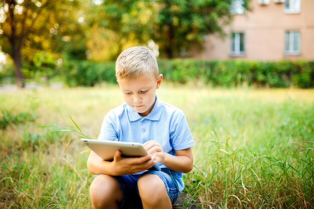 Dzieciak siedzi na dziedzińcu i gra w tablet na komputerze.