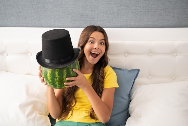 Dzieciak z owocami zdrowa żywność dla dzieci fruktoza zdrowe odżywianie na letnie wakacje nastolatka bawi się latem zaskoczona dziecko trzymaj arbuz arbuz w letnim cylindrze kapelusz