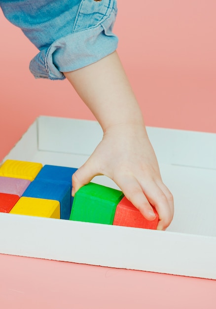 Dziecięca ręka bierze drewniane kolorowe kostki z białego pudełka.