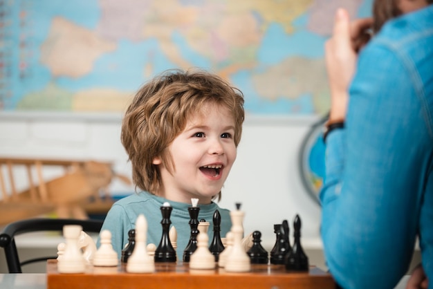 Dziecięca szkoła szachowa Wesoły uśmiechnięty chłopczyk siedzący przy stole i okazujący radość podczas gry w szachy