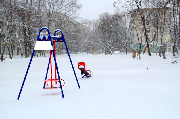 Dziecięce miejsce zabaw pokryte śniegiem w zimie Samotna huśtawka na placu zabaw dla dzieci podczas cyklonu śnieżnego Puste podwórko w europejskim mieście po opadach śniegu Konsekwencje cyklonu w Europie