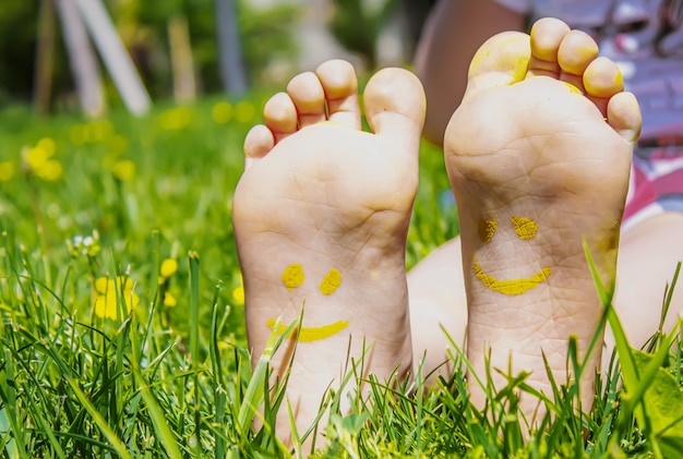 Dziecięce nóżki z wzorem farb uśmiechają się na zielonej trawie. Selektywne skupienie. Natura.