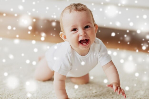 Zdjęcie dzieciństwo dzieciństwo i ludzie pojęcie szczęśliwy uśmiechnięty mały chłopiec lub dziewczyna czołgający się po podłodze w domu nad śniegiem