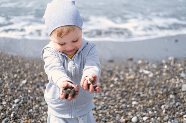 Dziecko blond chłopiec bawi się skałami i piaskiem na plaży w słoneczny dzień wiosną lub jesienią