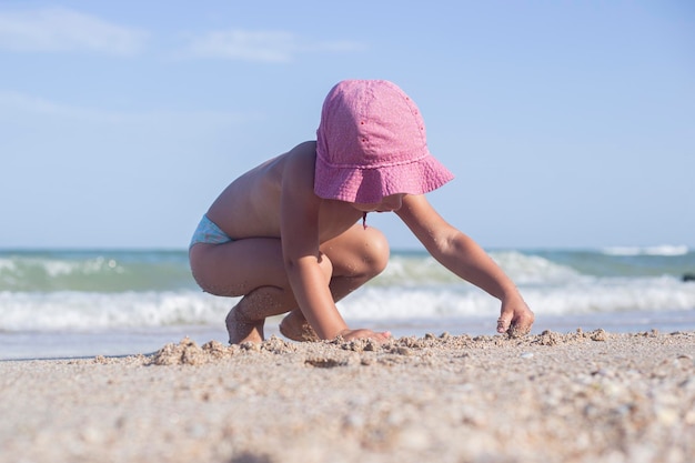 Dziecko blond dziewczyna bawi się piaskiem na plaży.