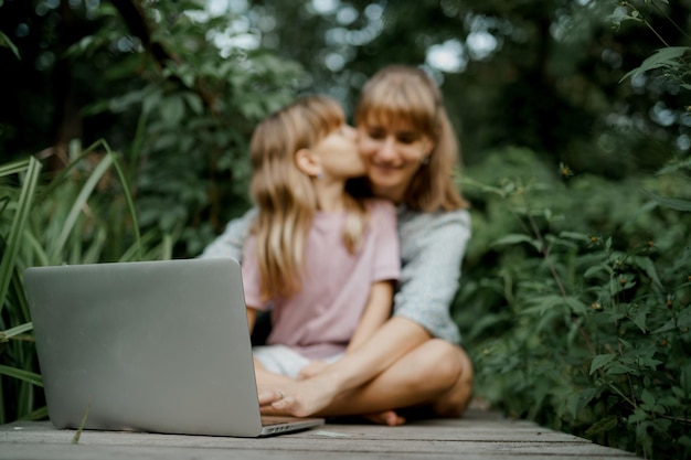 Zdjęcie dziecko całuje mamę podczas zabawy na laptopie w ogrodzie.