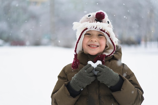 Dziecko cieszące się zimą chłopiec trzyma w rękach serce ze śniegu w zimowej koncepcji miłości