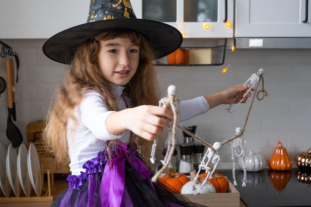 Dziecko dekoruje kuchnię w domu na Halloween Dziewczyna w stroju wiedźmy bawi się dekoracją na święta nietoperze jack lantern dynie Jesienny komfort w domu Skandynawska kuchnia na poddaszu