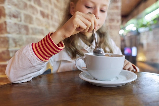 Dziecko dziewczynka 9, 10 lat z kubkiem gorącej czekolady, siedząc w kawiarni przy stole.