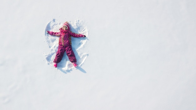 Zdjęcie dziecko dziewczynka bawić się anioła śniegu w śniegu i robić. płaski widok z góry