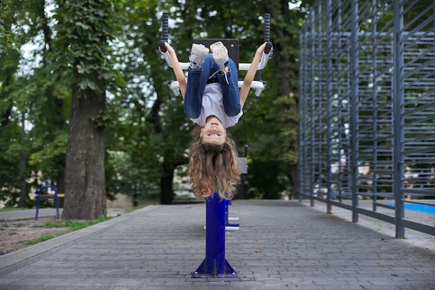 Zdjęcie dziecko dziewczynka na sportowym symulatorze na świeżym powietrzu, wisząca do góry nogami, aktywny zdrowy tryb życia dzieci, miejskie boiska sportowe