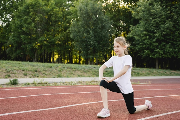 Dziecko dziewczynka rozgrzewa się na torze sportowym przed bieganiem