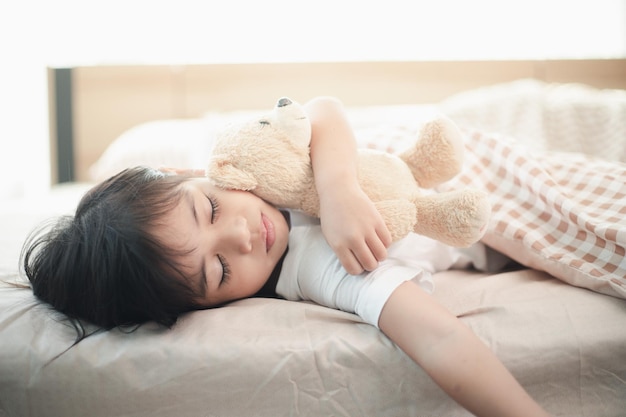 Dziecko dziewczynka śpi w łóżku z pluszowym misiem