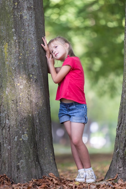 Dziecko dziewczynka stoi w pobliżu duży pień drzewa