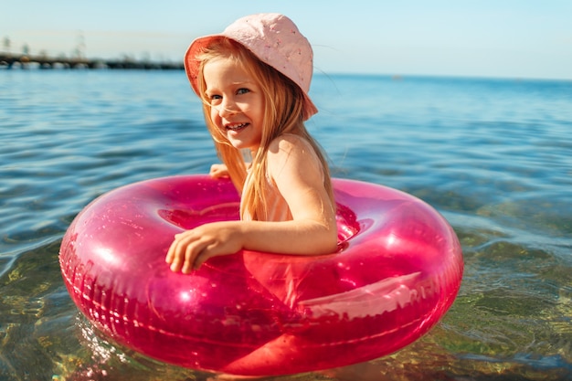 Dziecko dziewczynka w różowej panamie pływającej w morzu z okręgiem