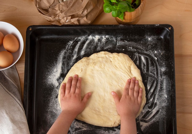 Dziecko formuje rękoma ciasto na pizzę w okrąg Gotowanie domowej pizzy